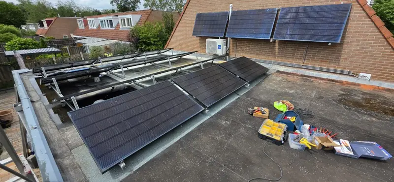 Zwarte zonnepanelen op een plat dak en tegen de gevel van een woning, tijdens de montage